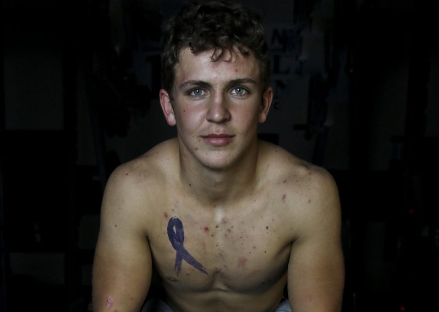 Junior Ethan Weidert sits in the weight room, his tattoo, which covers a port scar, exposed. Weidert was tattooed over the summer and selected a violet ribbon to represent Hodgkin lymphoma. Photo by Aubrey Bolinger