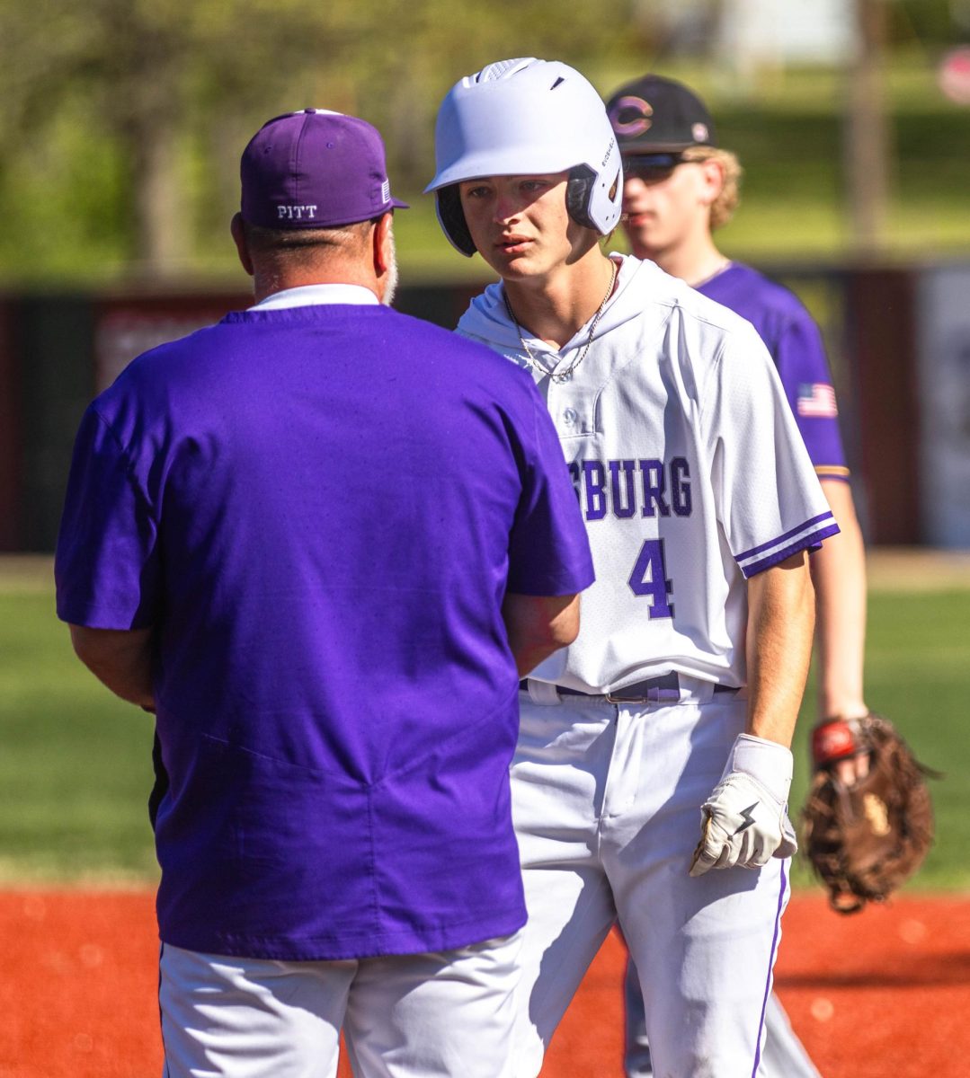 After hitting a ground ball to third base and beating the throw to first base, Coach Dwayne Vaughn congratulates  senior Beau Pasteur, and tells him how to score. 